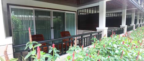A covered outdoor seating area with a glass partition, wooden chairs, and a view of the building's interior.