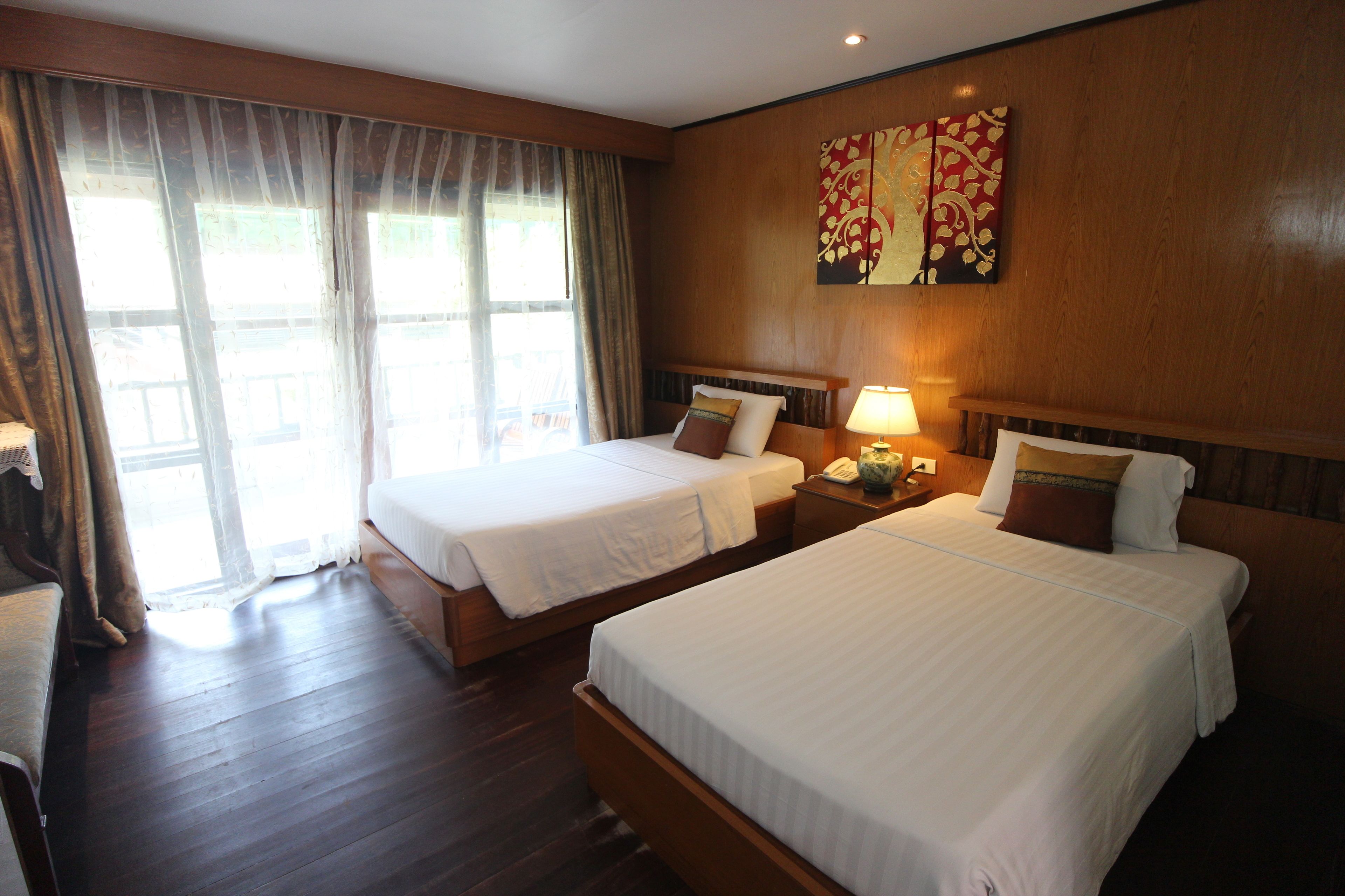 Habitación de hotel con dos camas, piso de madera, un ventanal grande con cortinas y una obra de arte colgada en la pared.