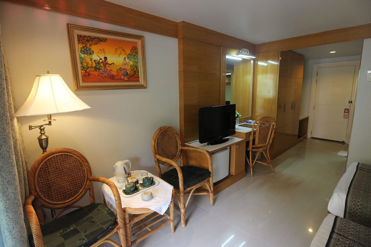 A hotel room with a television, wicker chairs, a small table with a tea set, and a painting on the wall.