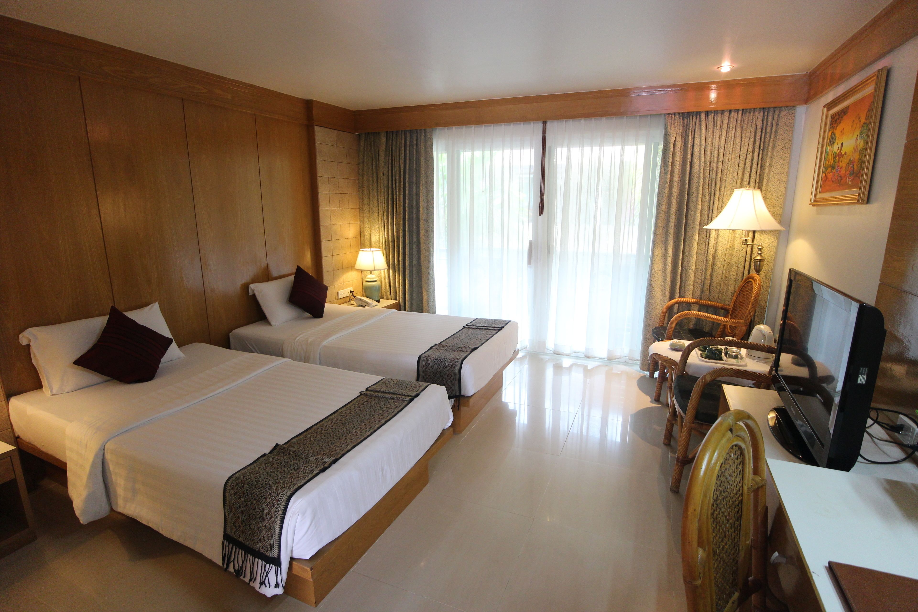 Habitación de hotel con dos camas, un escritorio, una silla, un televisor y una ventana con cortinas.