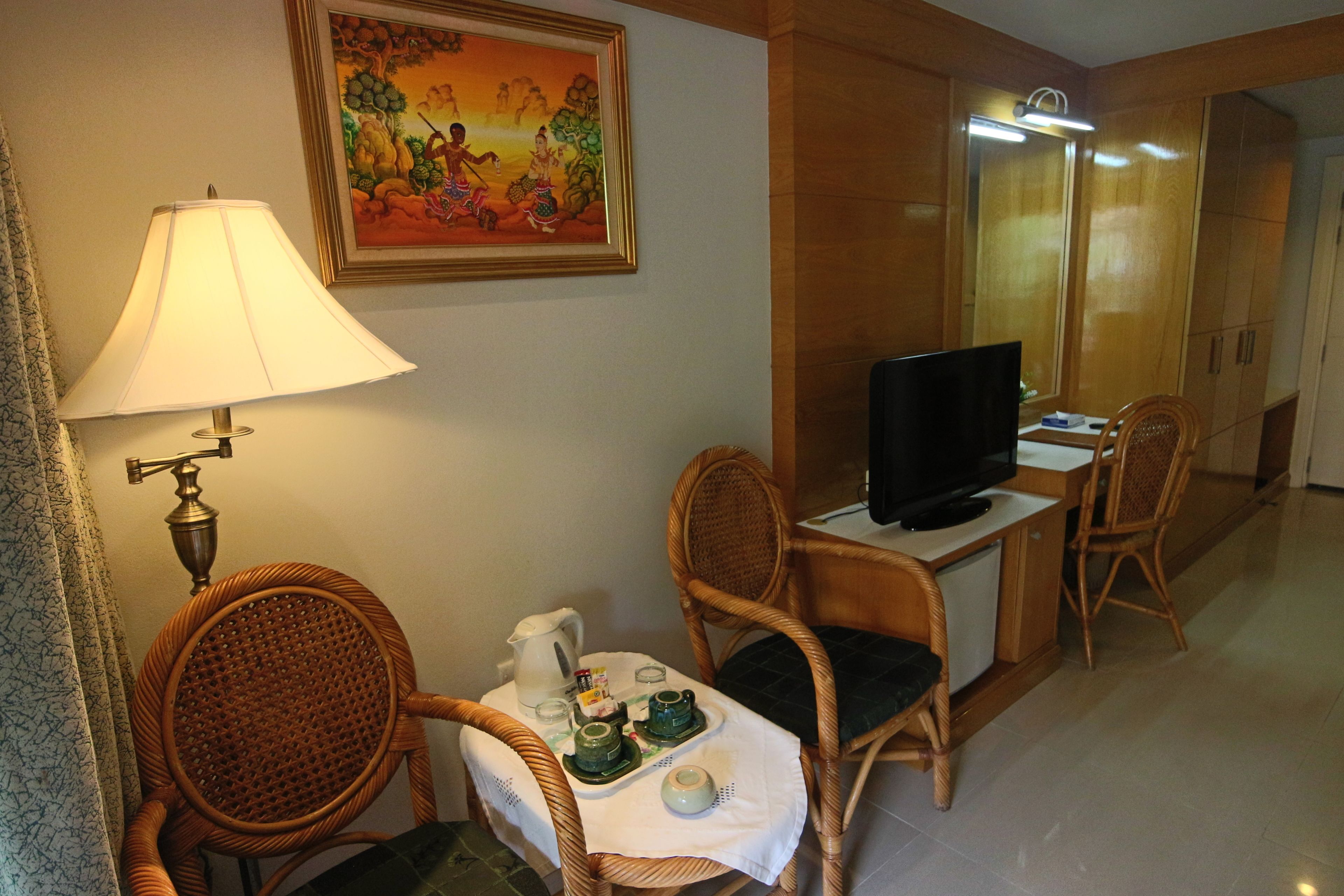 A hotel room with wicker chairs, a television, a table with a tea set, and a painting on the wall.