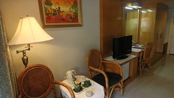 A hotel room with wicker chairs, a television, a table with a tea set, and a painting on the wall.
