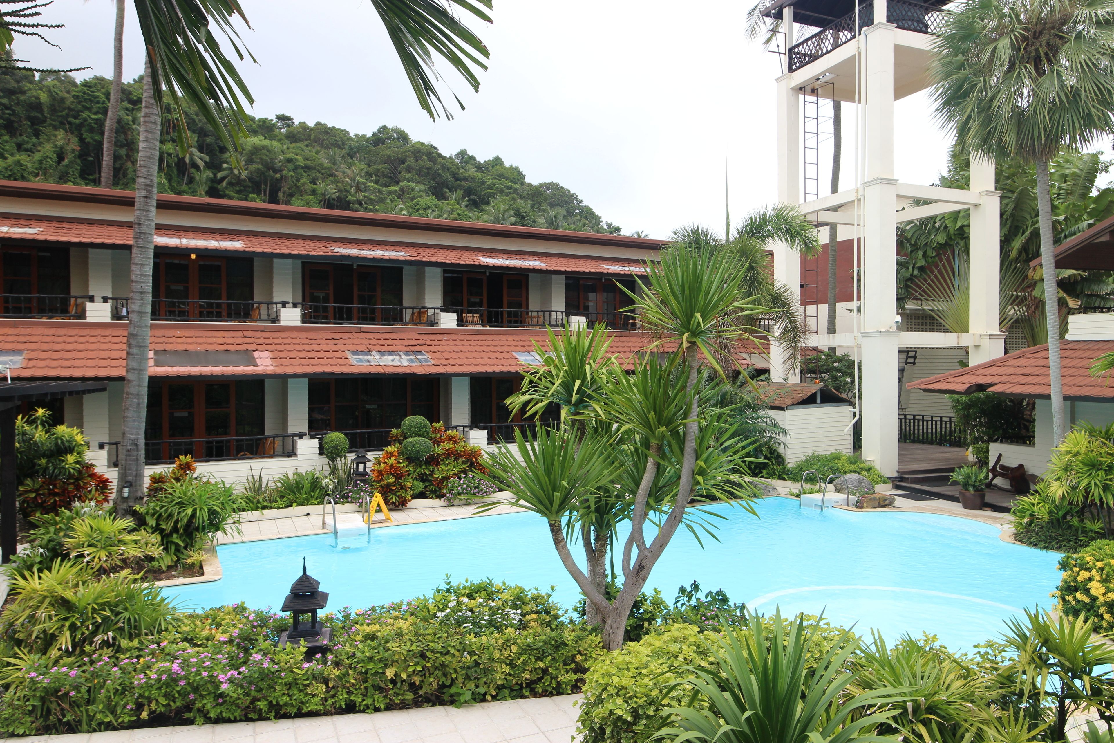 A hotel with a swimming pool surrounded by tropical plants and a multi-story building with balconies.