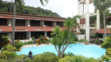 Un hotel con piscina rodeado de plantas tropicales y un edificio de varios pisos con balcones.