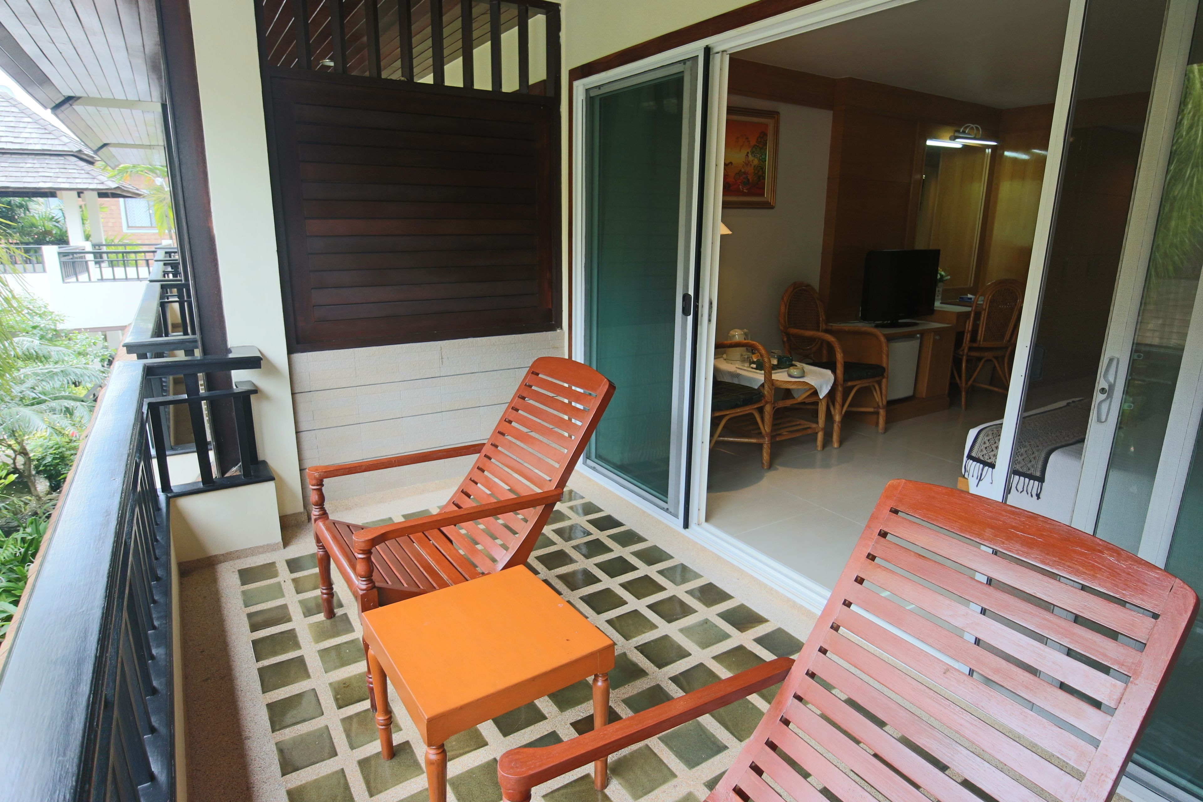 A balcony with wooden furniture, a tiled floor, and a sliding glass door leading to a room with a television and seating.
