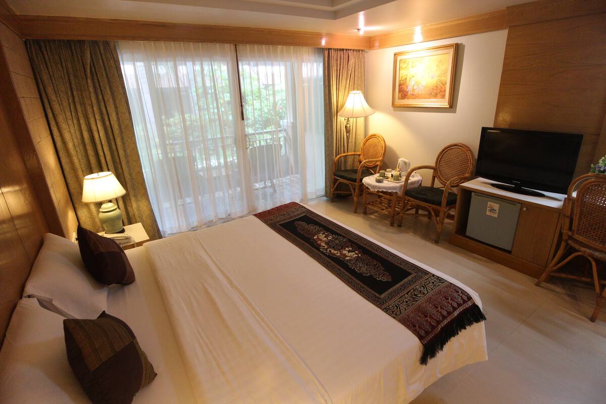 A hotel room with a large bed, a television, a desk with a chair, and a window with curtains.