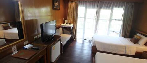 A hotel room with two beds, a desk with a television, a small table with a coffee maker, and a window with curtains.