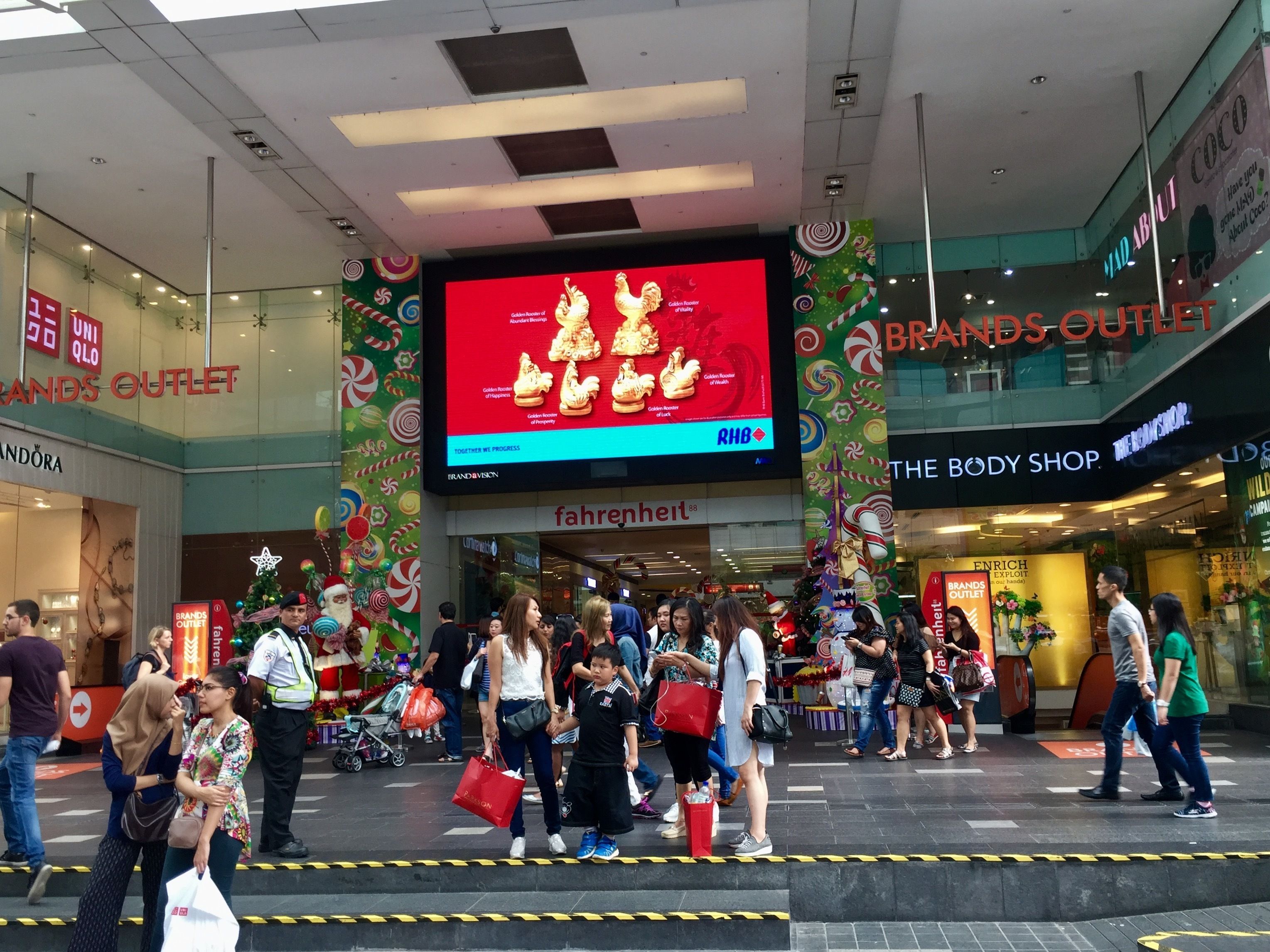 A shopping mall with a large digital advertisement for a brand outlet.
