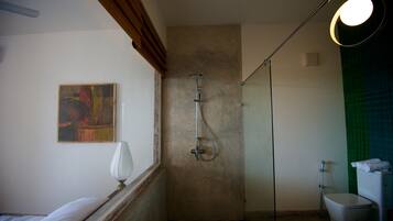 A bathroom with a shower, a toilet, a bed, and a painting on the wall.