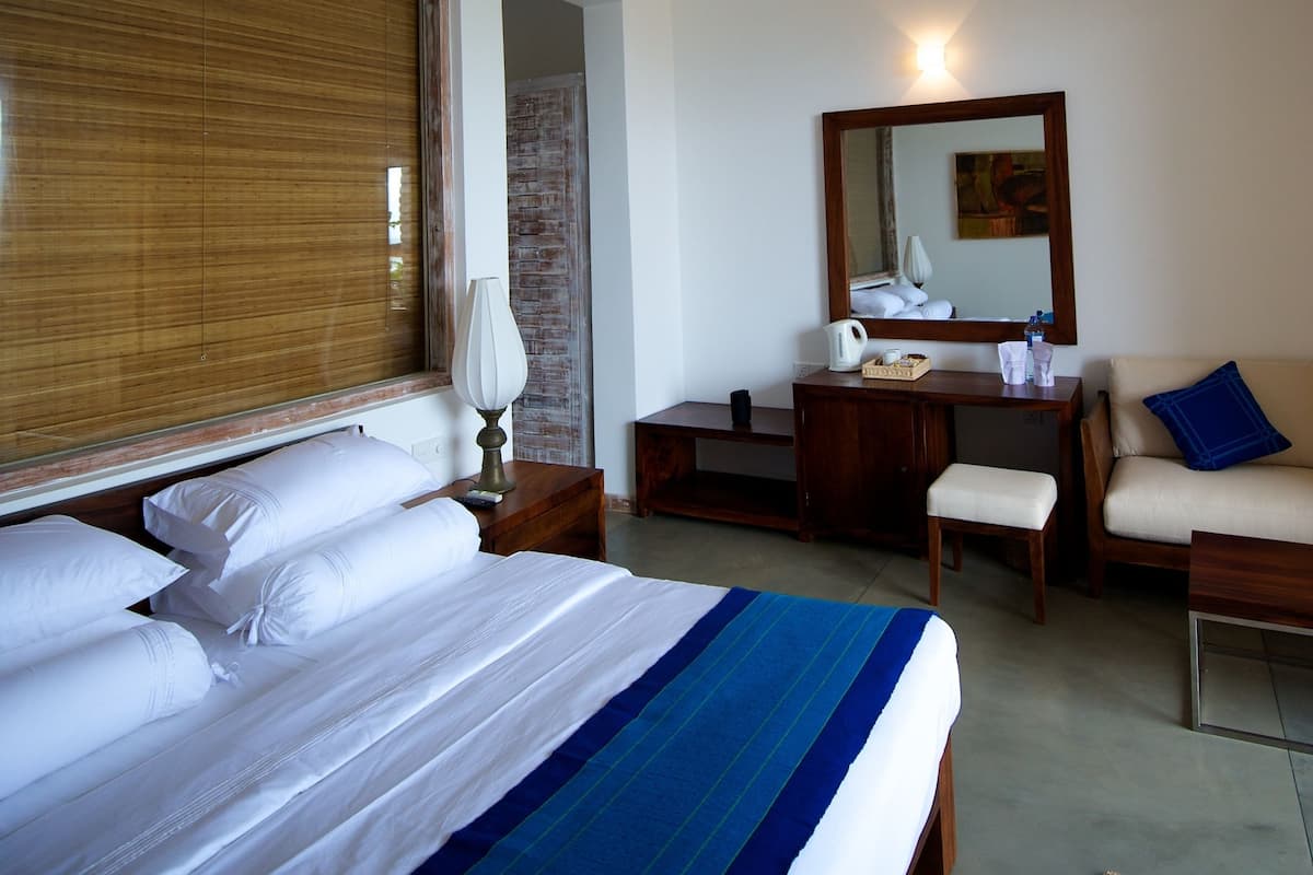 Habitación de hotel con cama, escritorio, silla, ventilador de techo, espejo y ventana con persianas.