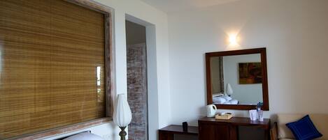 A hotel room with a bed, a desk, a chair, a ceiling fan, a mirror, and a window with blinds.