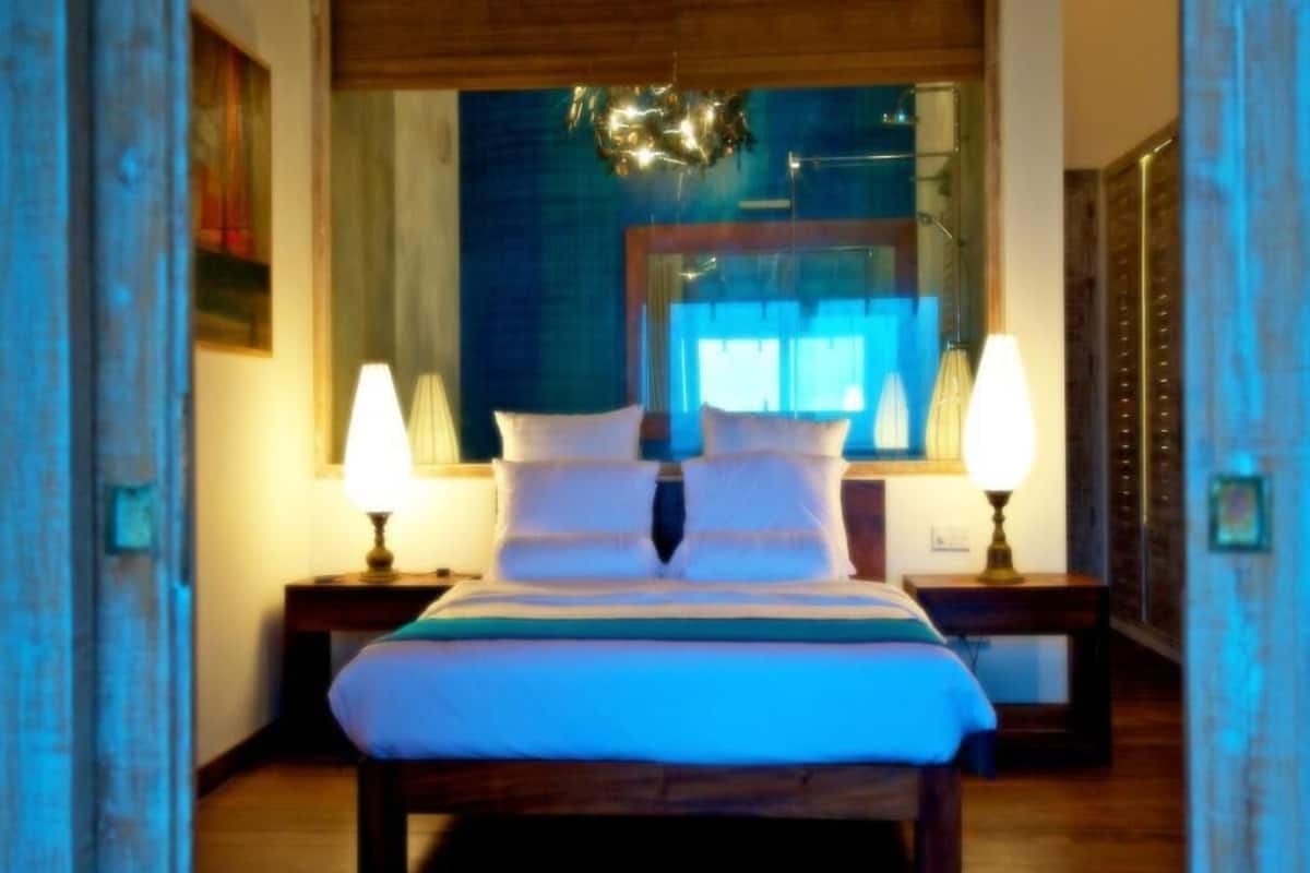 Una cama con dos mesitas de noche, un espejo sobre la cama y vistas al exterior a través de una ventana.