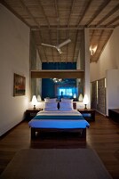 Un dormitorio con una cama grande, dos mesitas de noche con lámparas, un ventilador de techo y vistas amplias a través de un ventanal.