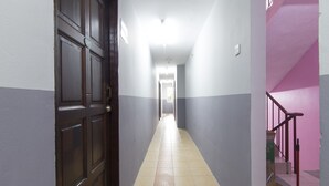 A hallway with a wooden door, a tiled floor, and a staircase with a pink wall.