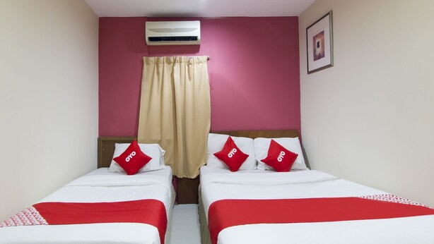 A hotel room with two beds, beige curtains, red pillows, and an air conditioning unit on the wall.