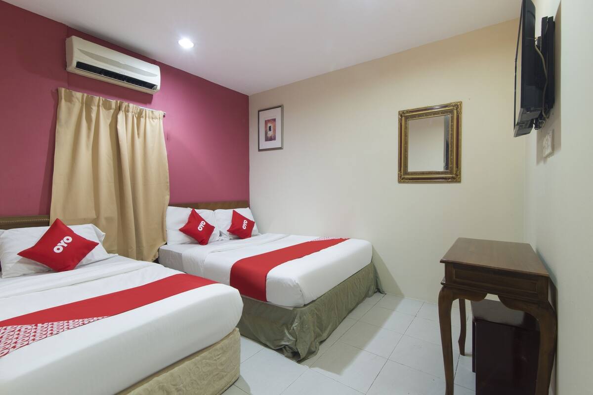 A hotel room with two beds, a desk, an air conditioner, a TV, and a framed picture on the wall.
