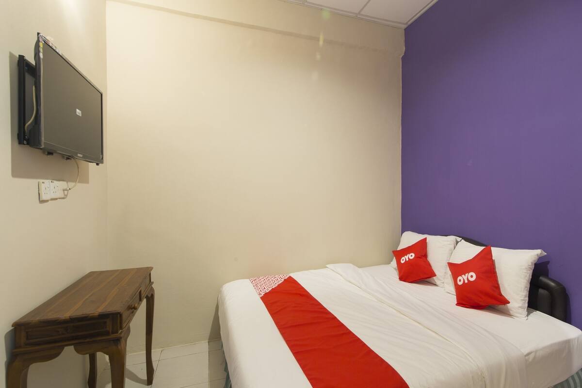 A room with a bed, a TV mounted on the wall, and a wooden table.