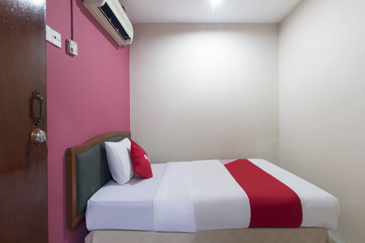 A single bed with white and red bedding, a wooden headboard, and a pink wall.