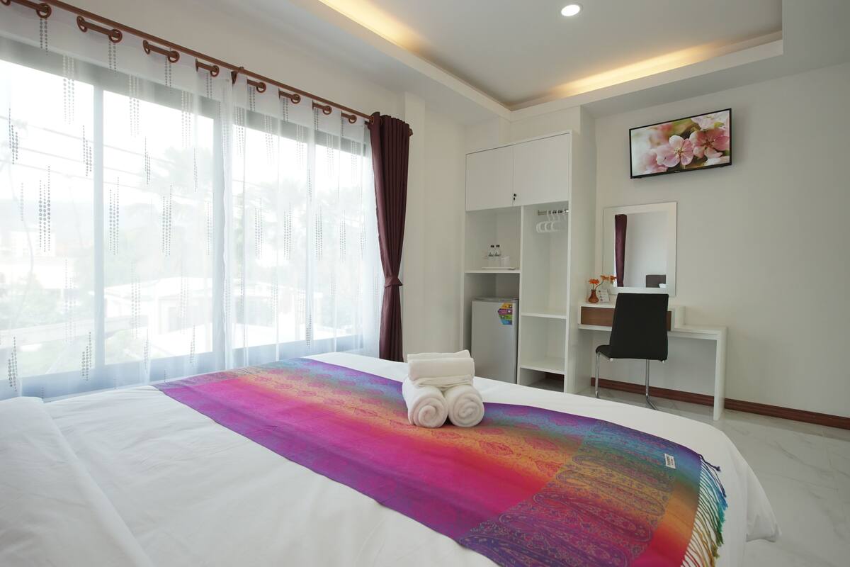 A hotel room with a large bed, a desk, a wardrobe, and a window with curtains.