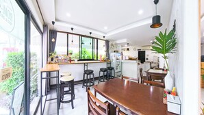 A modern kitchen with a dining area, large windows, and a view of greenery outside. - Gusto House (Chiang Mai)