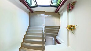 A spiral staircase with a glass ceiling, white walls, and a wall-mounted flower arrangement. - Gusto House (Chiang Mai)