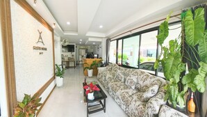 A modern living room with a sofa, a coffee table, and potted plants. A reception desk is visible in the background. - Gusto House (Chiang Mai)