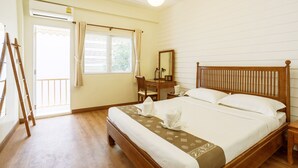 Une chambre d’hôtel avec un lit en bois, un bureau avec une chaise, une fenêtre avec des rideaux et un appareil de climatisation.