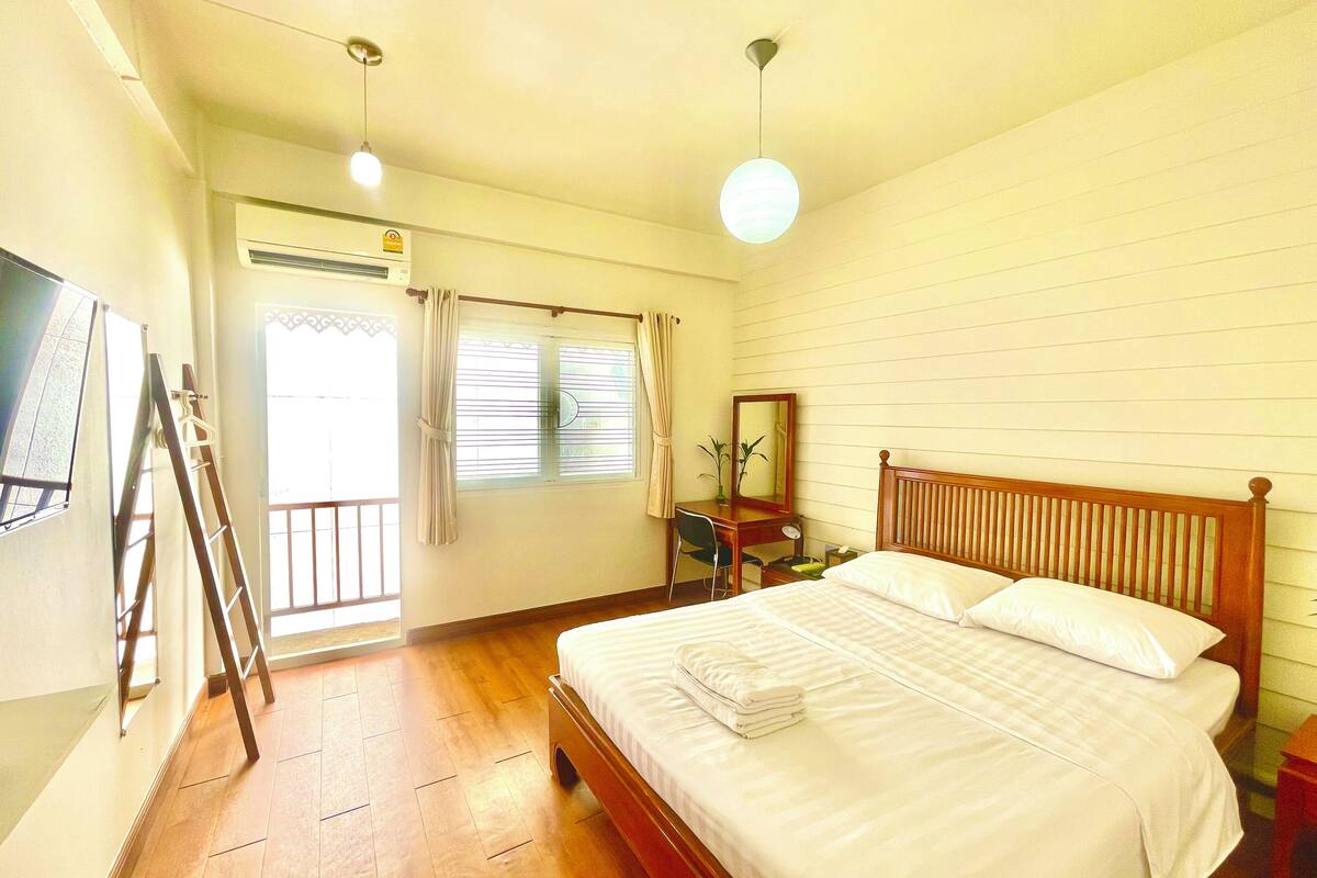 Une chambre d’hôtel avec un lit en bois, un bureau avec une chaise, un miroir et une fenêtre avec des rideaux.