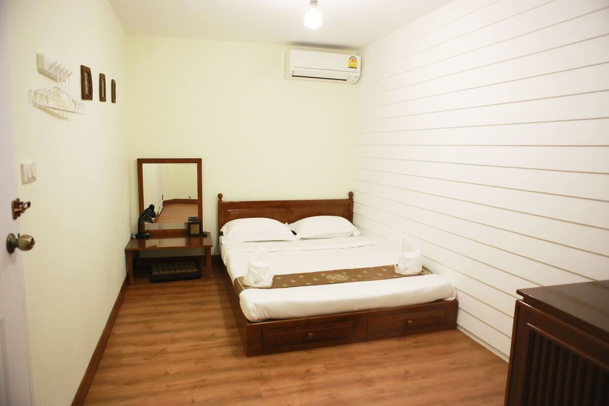 Une chambre à coucher avec un lit en bois, une table de chevet, un miroir, un appareil de climatisation et une porte.