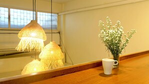Une pièce avec un plancher en bois, un mur blanc, une fenêtre donnant sur un beau paysage, deux lampes suspendues et un vase rempli de fleurs.