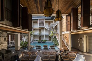 Un área de piscina interior con sillones de madera, una piscina central y una escalera que conduce a plantas superiores.
