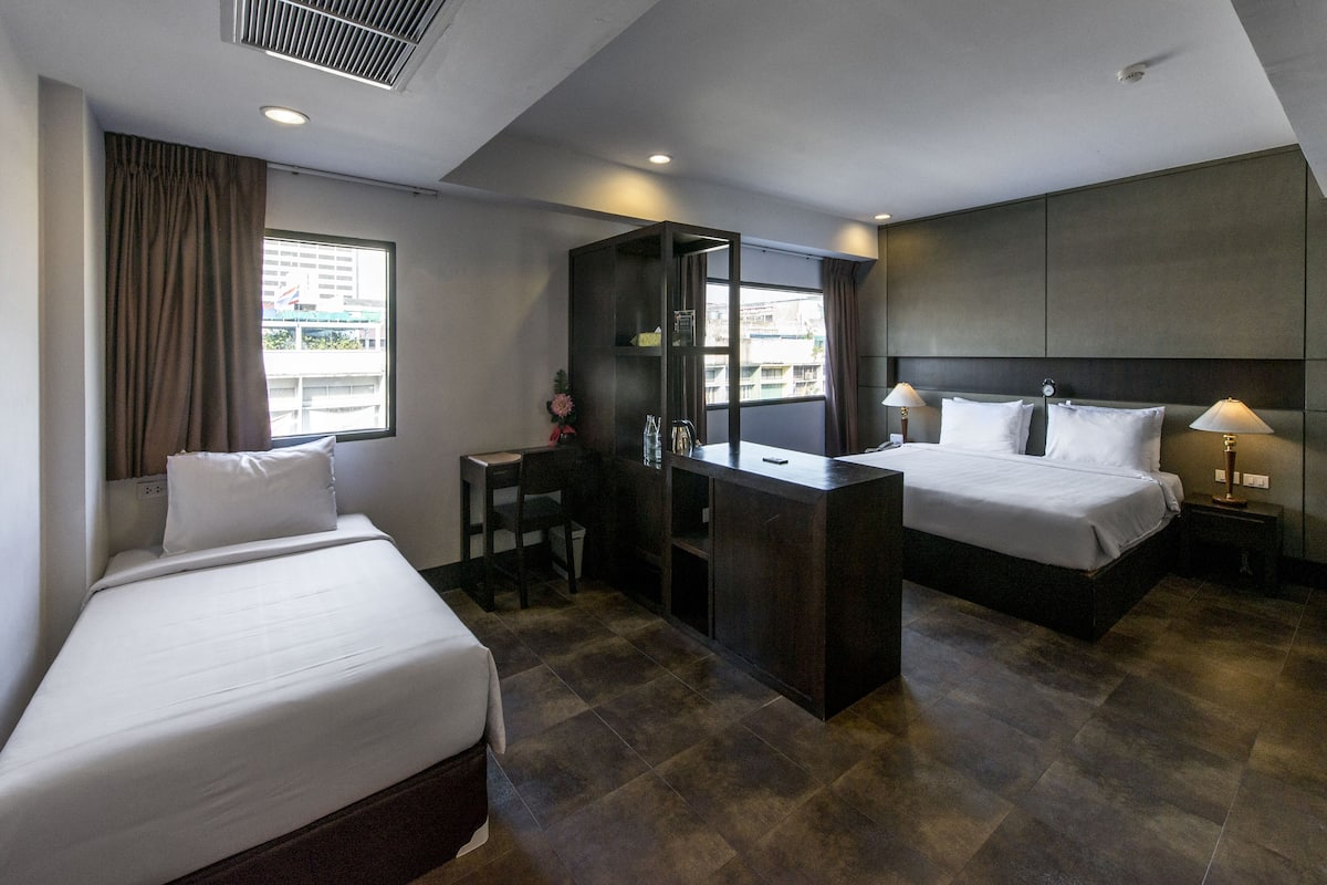 A hotel room with two beds, a desk, a minibar, and a view of the city.