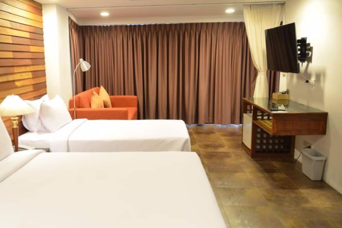 A hotel room with two beds, a desk, a TV, and a window with curtains.