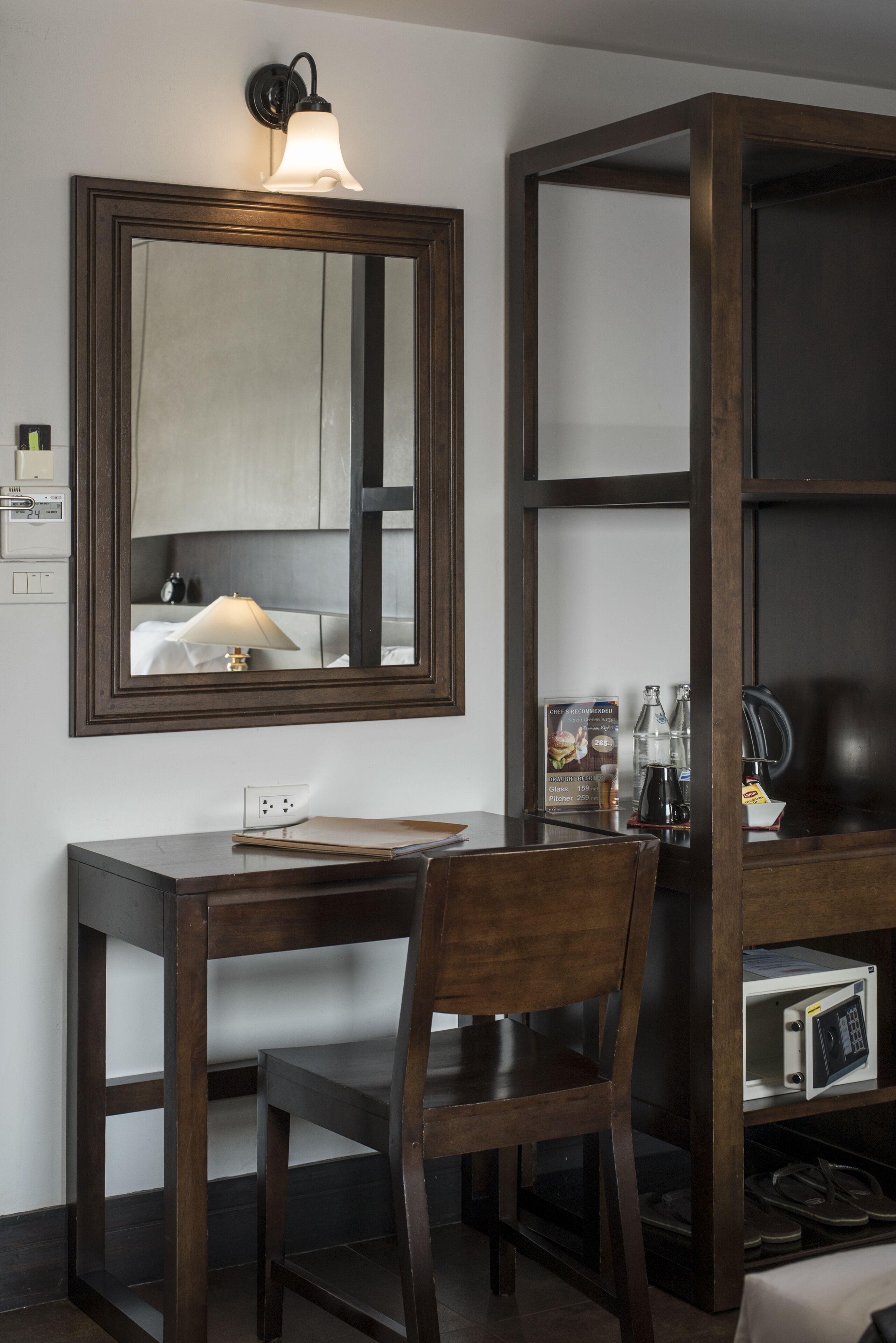 A hotel room with a wooden desk, chair, and a large mirror above the desk. There is a shelf with a microwave and a coffee maker on it.