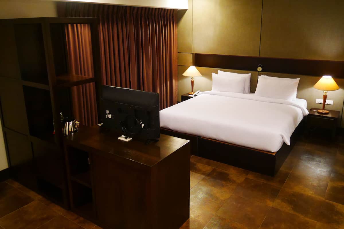 A hotel room with a bed, two bedside lamps, a TV, and a wooden desk.