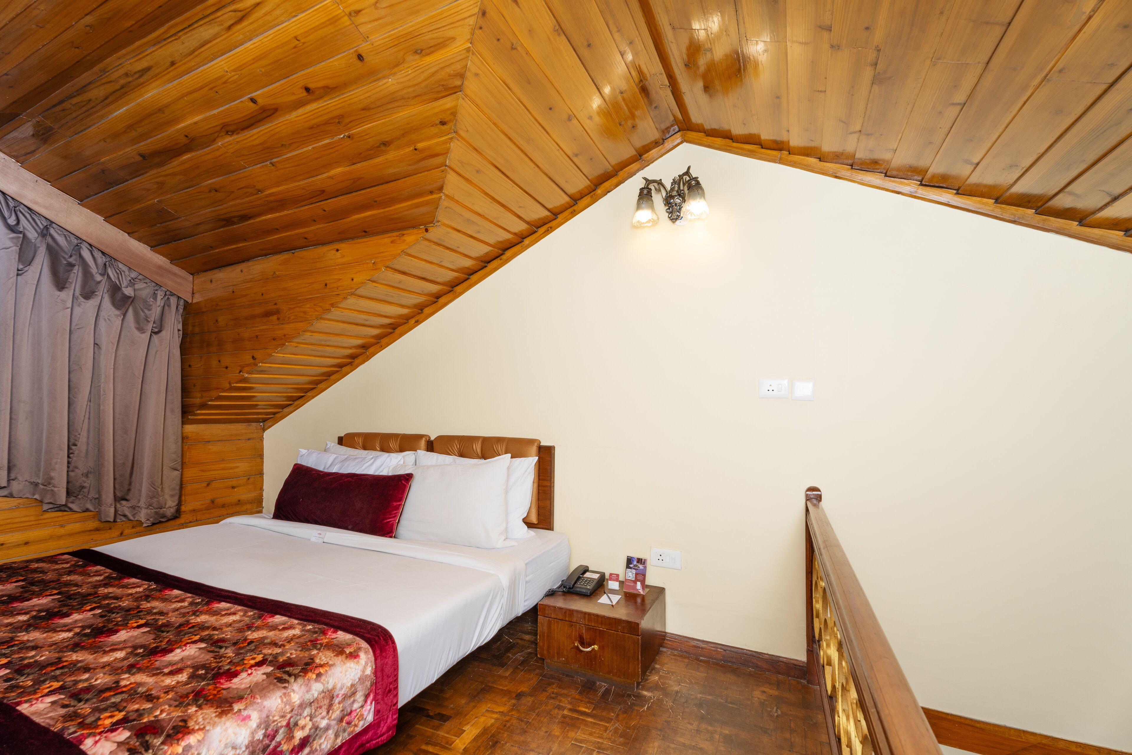 Un dormitorio con techo de madera, una cama con ropa blanca, una mesita de noche e iluminación fijada a la pared.