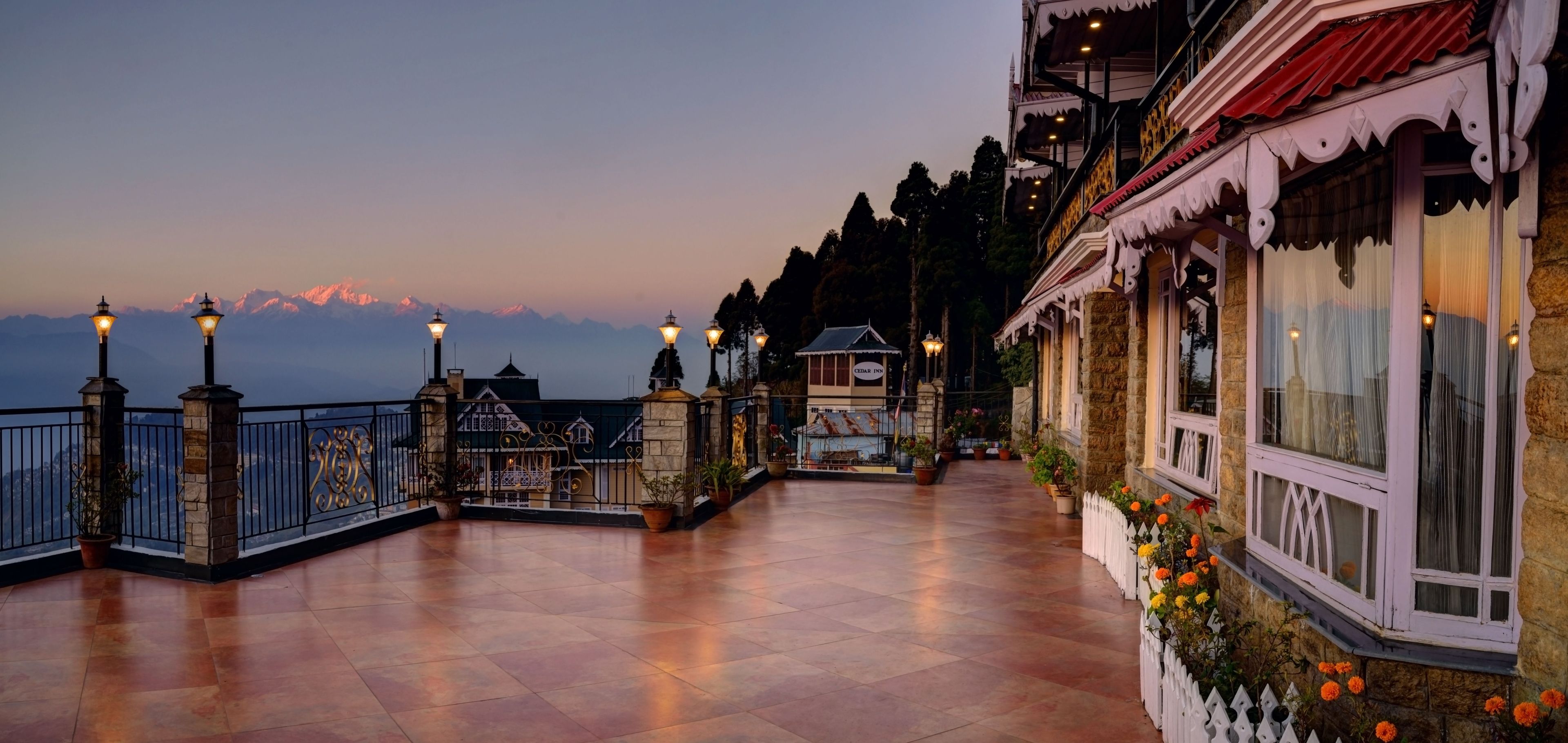 Une terrasse d’hôtel offrant une vue sur les montagnes, un bâtiment en pierre avec un toit rouge et une clôture blanche en bois.