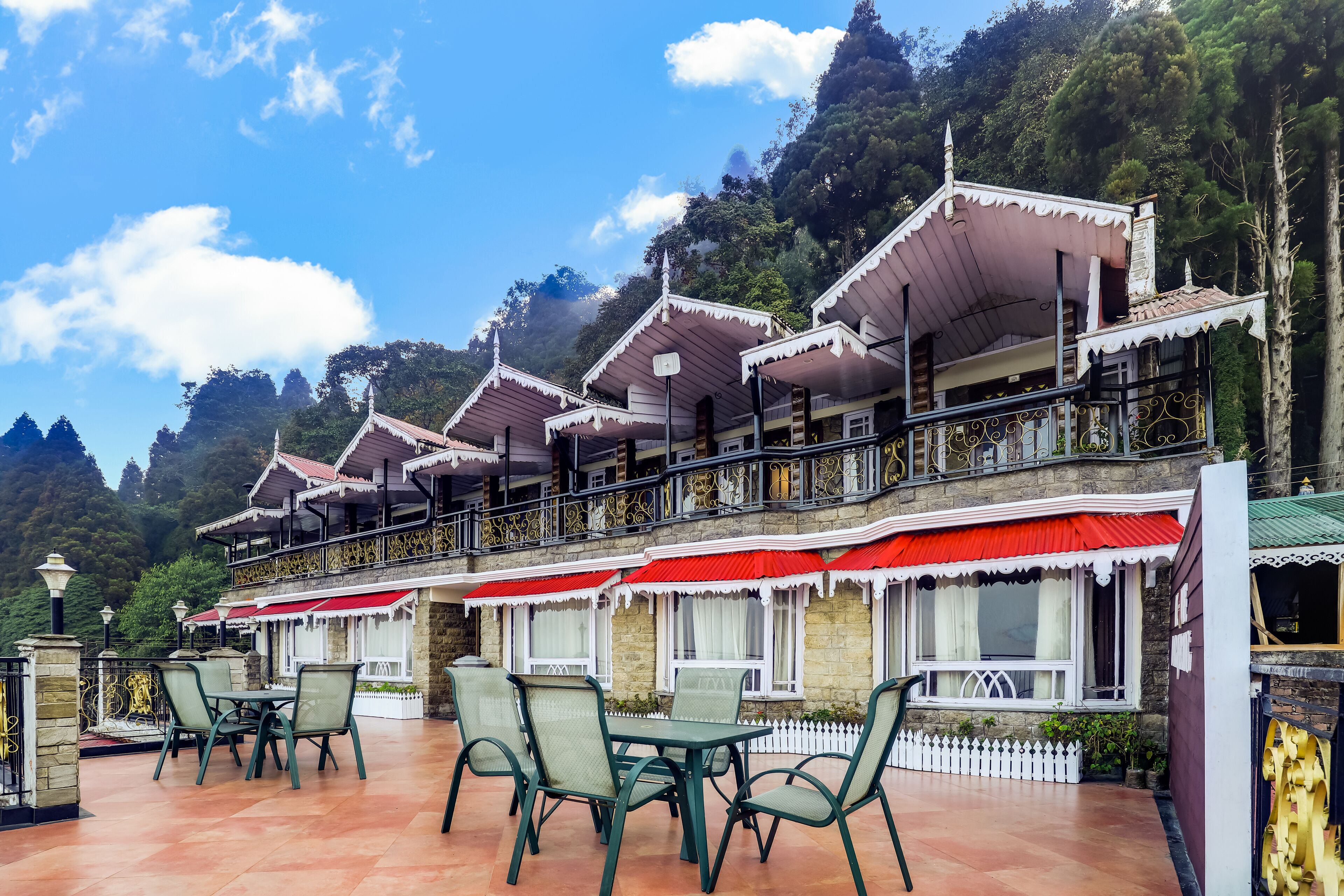 A traditional building with multiple balconies and red awnings, surrounded by lush greenery and mountains.