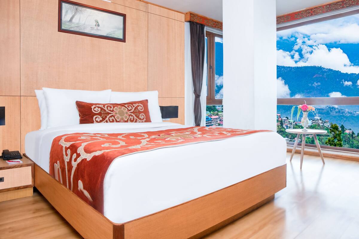 A modern hotel room with a large bed, a nightstand, a telephone, and a view of a mountainous landscape.