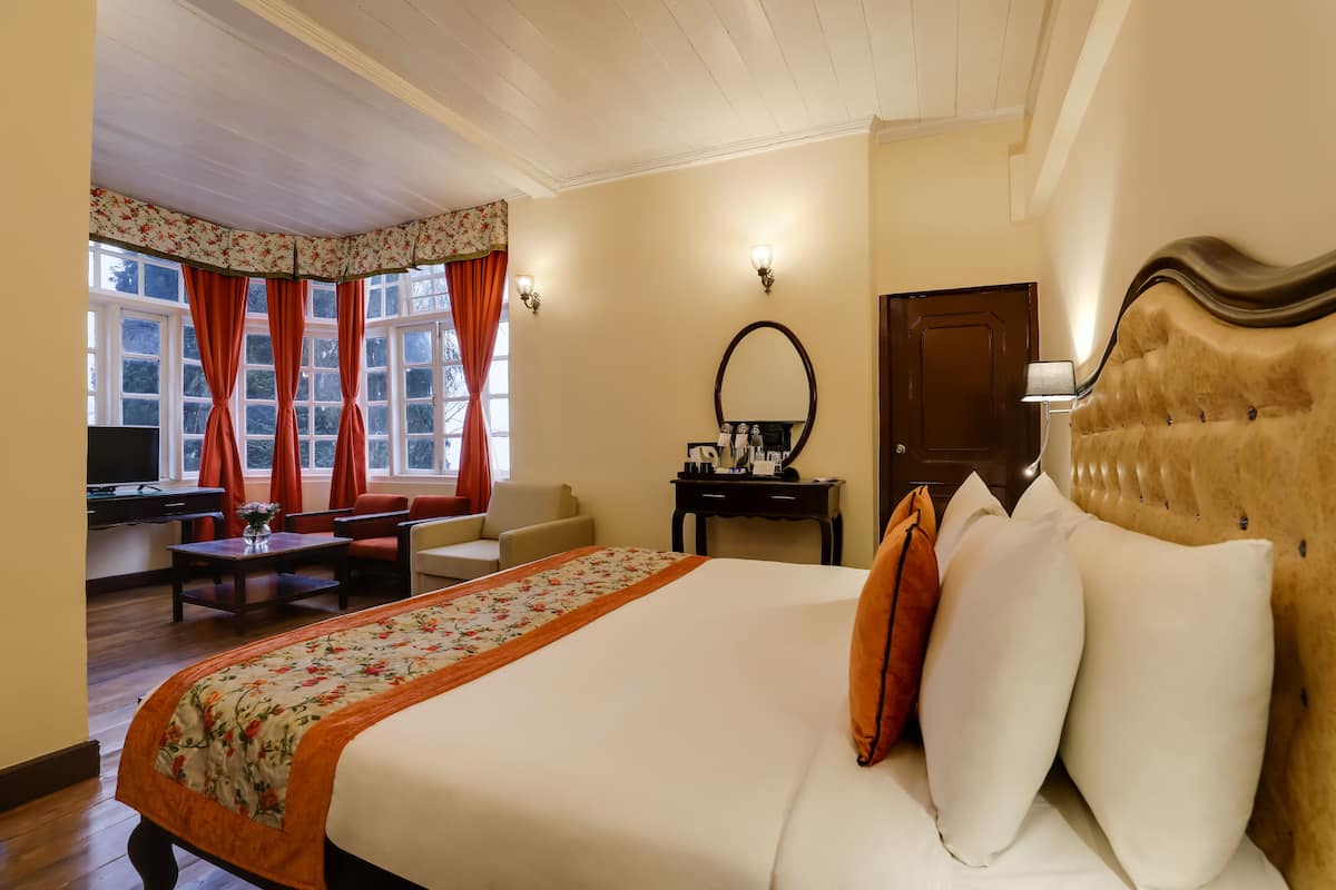 A hotel room with a large bed, a desk, a chair, a television, and a window with curtains.