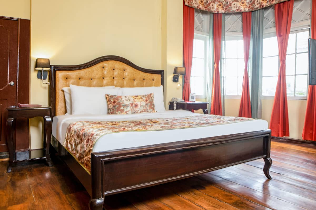 A large bed with a wooden headboard, two bedside tables, a telephone, and a television on a stand.
