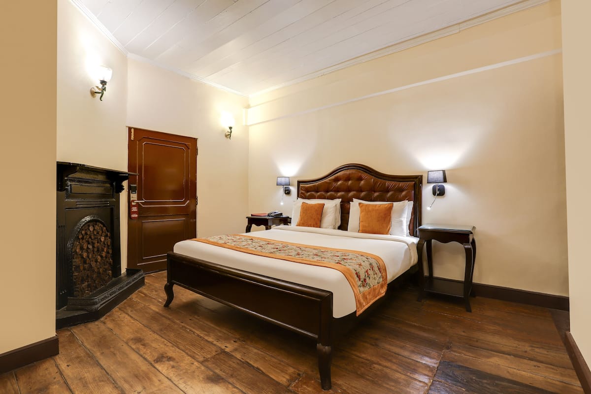 A bedroom with a wooden bed, a nightstand, a dresser, and a wall-mounted lamp.