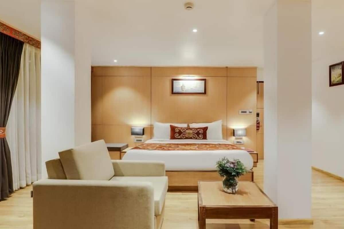 A hotel room with a bed, a sofa, a small table, and a nightstand with a lamp.