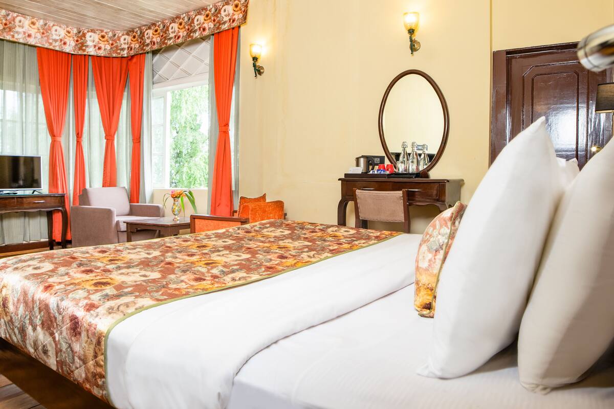 A hotel room with a bed, a desk, a chair, a television, and a window with curtains.