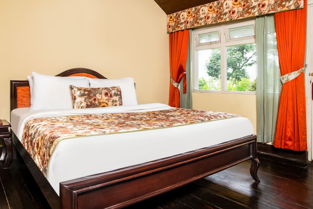 A neatly made bed with a floral bedspread, a wooden headboard, and a nightstand with a book and a lamp.