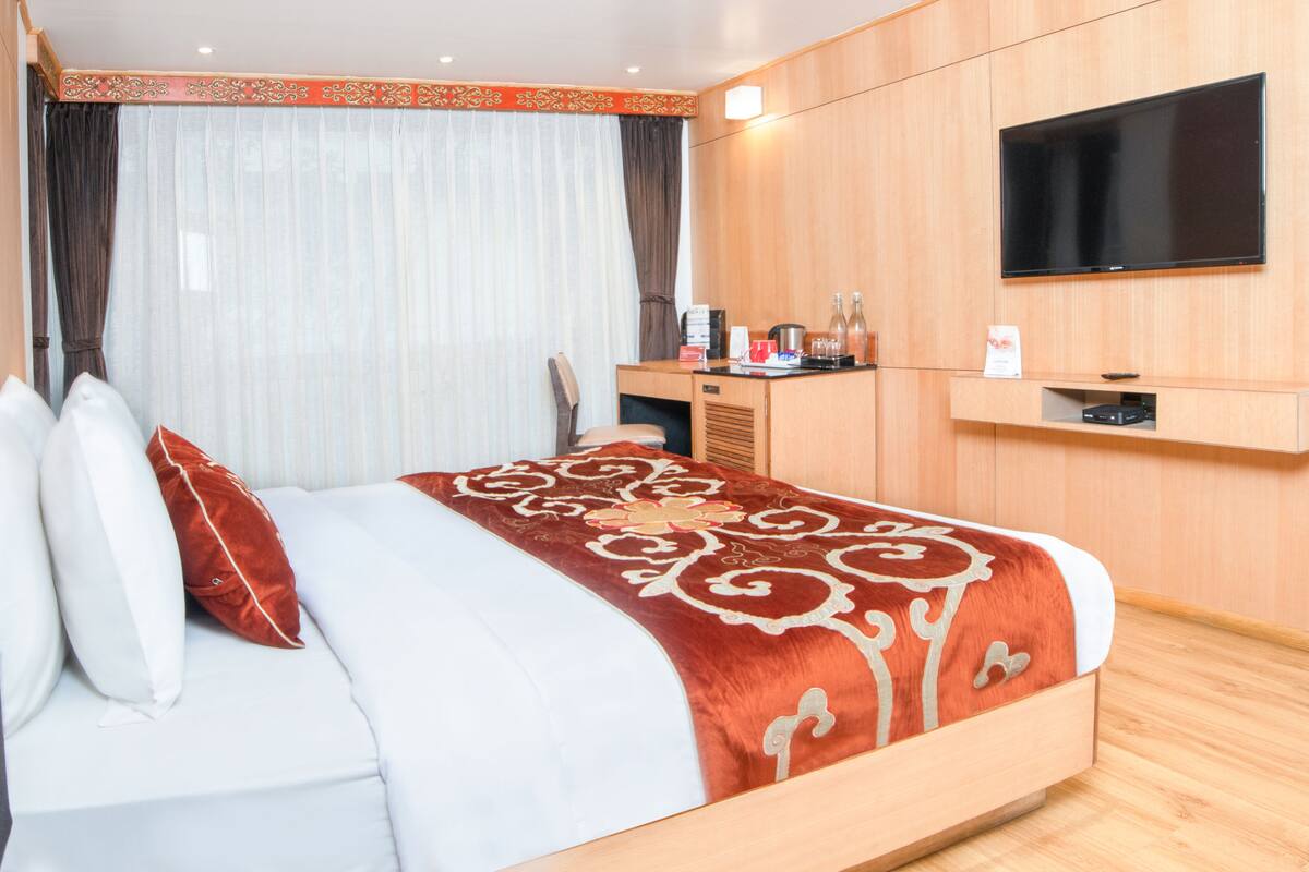 A hotel room with a bed, a desk, a flat-screen TV, and a minibar.