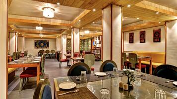 A spacious dining area with multiple tables and chairs, wooden ceiling beams, and a chandelier.