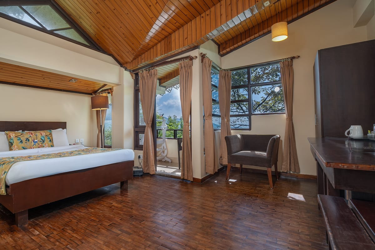 A bedroom with a wooden ceiling, a bed with floral bedding, a chair, and a desk with a cup.