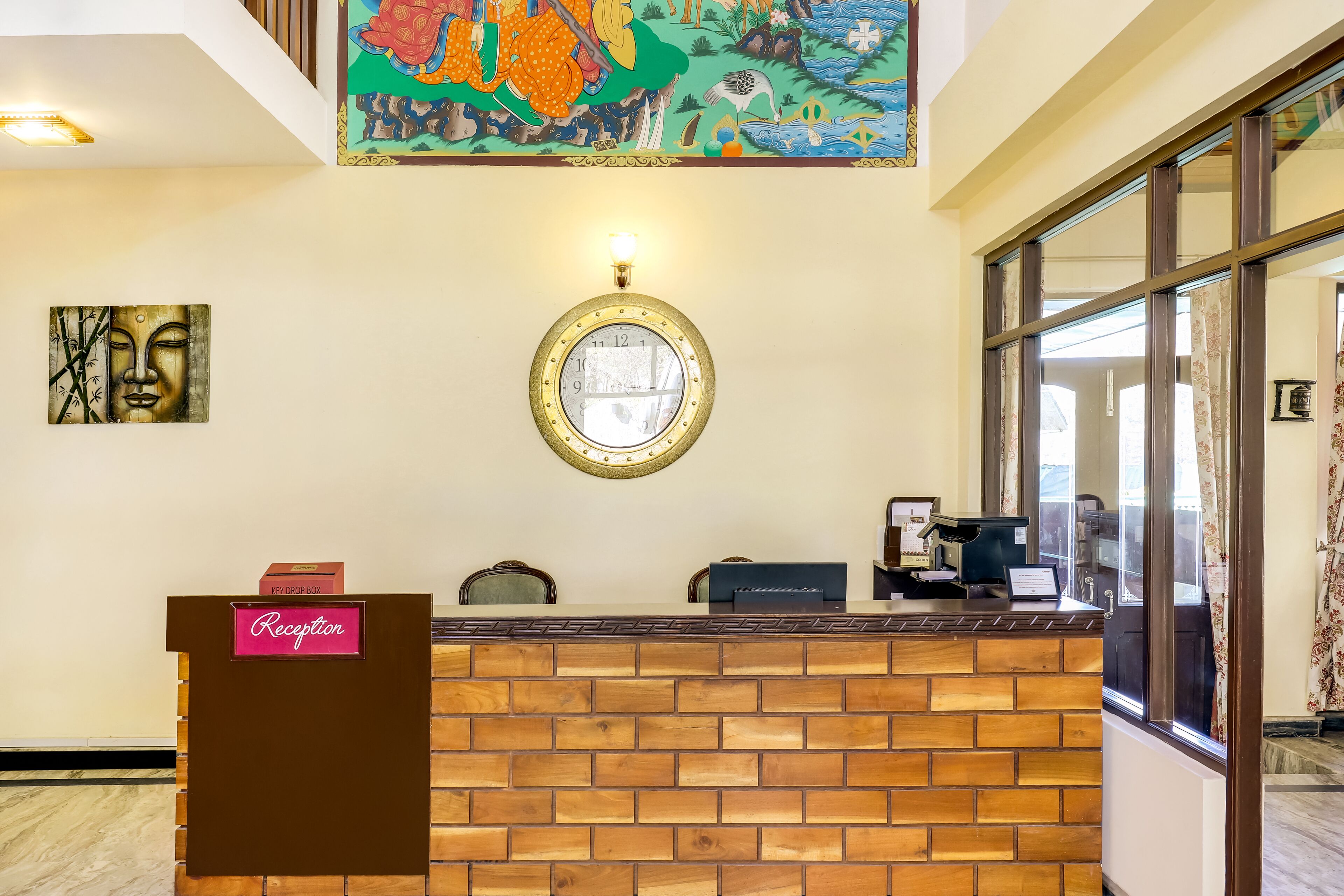 Un mostrador de recepción con fachada de ladrillo, un reloj encima y un mural colorido en la pared.