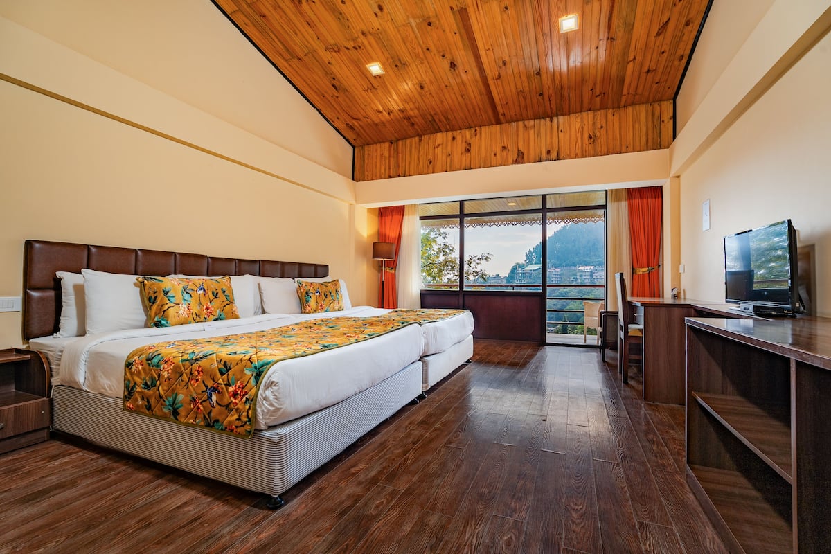 A spacious bedroom with a large bed, wooden ceiling, and a TV on a desk.